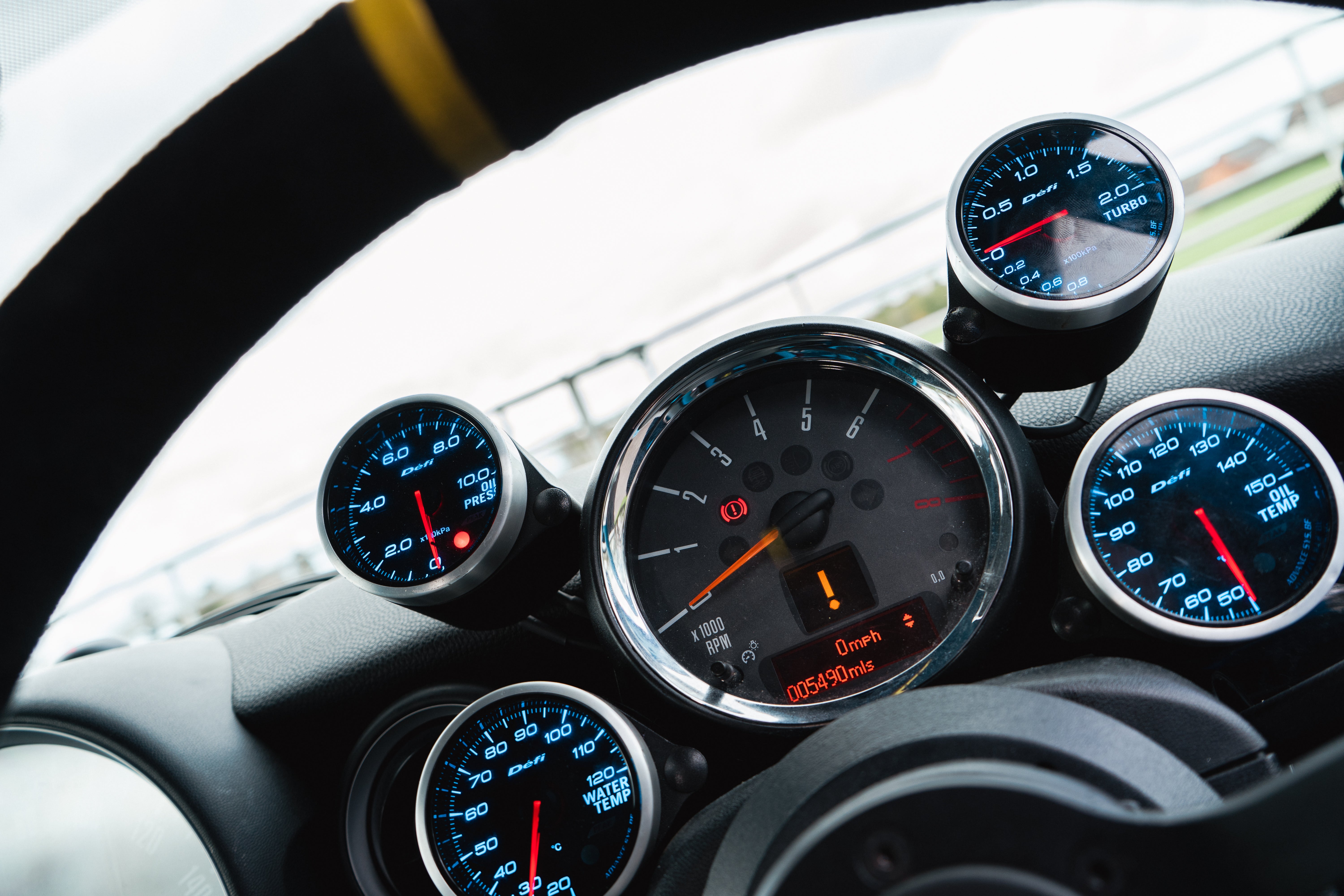 R56 with custom Defi guages around the rev counter. Water temperature guage, Oil Temp guage, boost pressure and oil pressure guiages all visable.